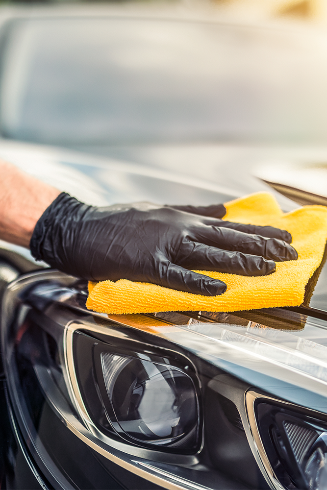 Una mano con un guante limpiando con una bayeta el faro de un coche